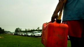 A person carrying a red plastic gas can on the side of the road