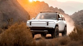 A white Rivian R1S driving through the desert at sunset