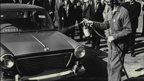 Businesspeople watch a worker use a spray car wax on a vehicle in 1964