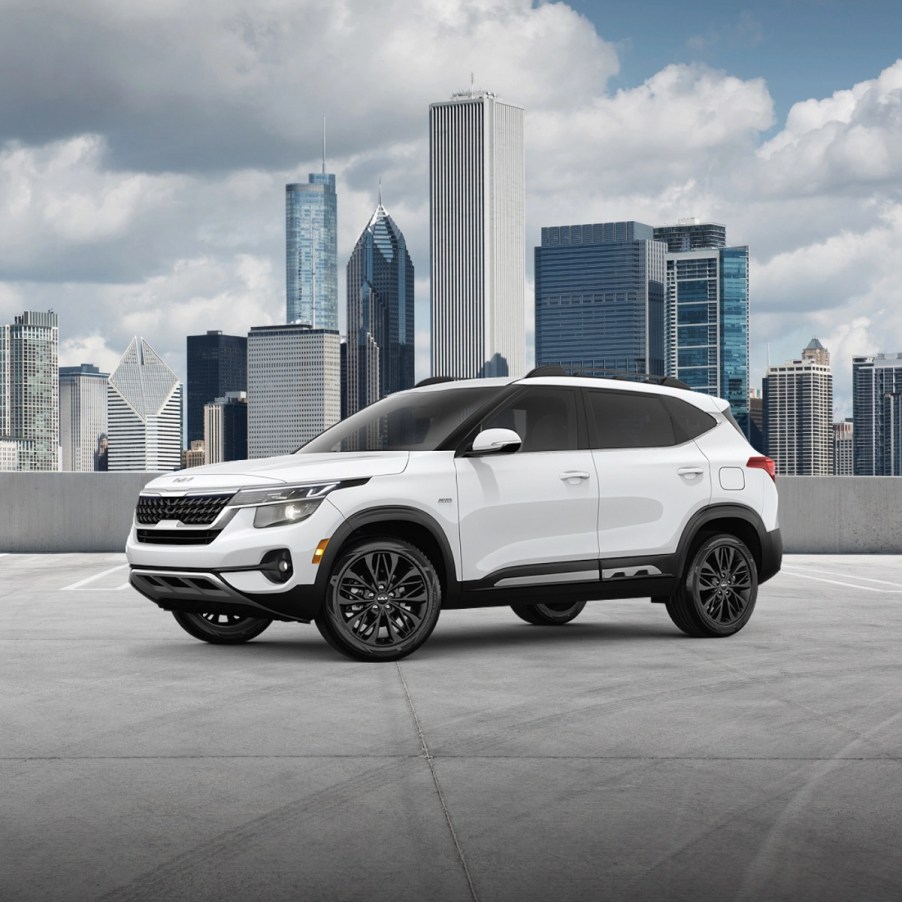 A white 2022 Kia Seltos on the top of a parking garage with a city in the back.