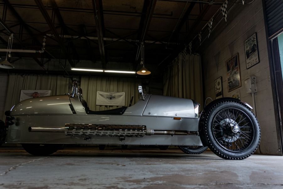 A low-angle side view of a silver 2012 Morgan 3-Wheeler in a garage