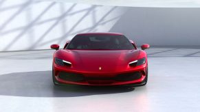 A red 2021 Ferrari 296 GTB parked on a white floor in front of a white wall and a sunny sky