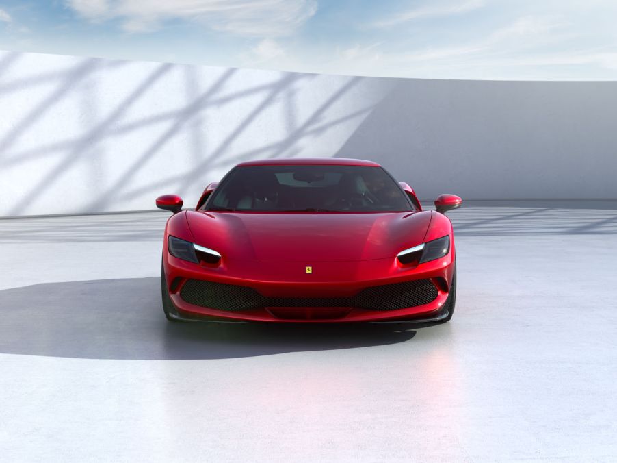 A red 2021 Ferrari 296 GTB parked on a white floor in front of a white wall and a sunny sky