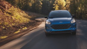 A blue metallic 2021 Ford Escape compact SUV travels on a tree-lined, sun-dappled country road