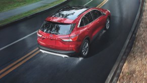 A red 2021 Ford Escape travels on a wet two-lane highway. The Ford Escape hybrid is one of five SUVs with the best gas mileage, according to CarGurus.