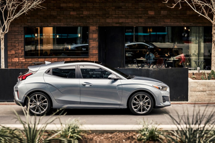 A silver 2021 Hyundai Veloster parked in front of a storefront