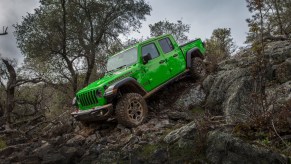 A 2021 Jeep Gladiator Rubicon in Gecko Green parked on the edge of a rocky incline on a cloudy day