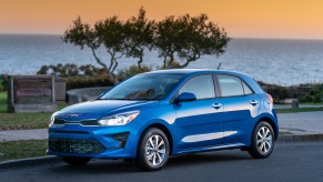 A blue metallic 2021 Kia Rio 5-Door Hatchback parked on a street overlooking a body of water at sunset