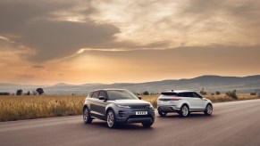 Two 2021 Land Rover Range Rover Evoque luxury compact SUVs parked on a road through a plain in front of mountains