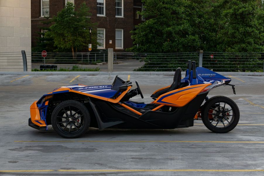 The side view of a blue-and-orange 2021 Polaris Slingshot R in a parking lot