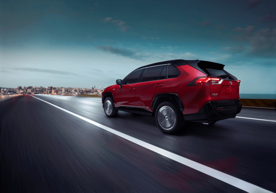 The 2021 Toyota RAV4 Prime PHEV SUV in dark red driving down a highway toward an urban city