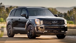 A black 2022 Kia Telluride in a wooded mountainous area on a concrete drive.