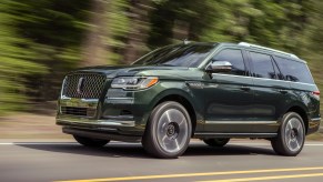 A 2022 Lincoln Navigator Manhattan Green Black Label traveling on a two-lane highway passing a blur of trees