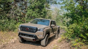 A mud-colored 2022 Nissan Frontier traveling on a dirt road up a hill