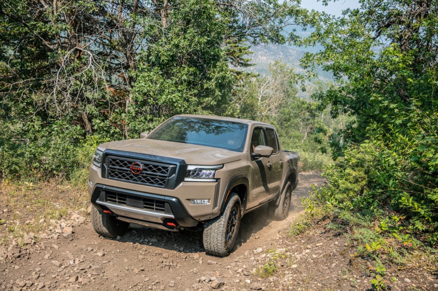 A mud-colored 2022 Nissan Frontier traveling on a dirt road up a hill