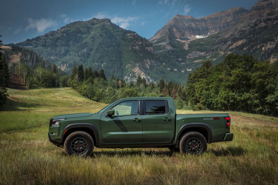 The 2022 Nissan Frontier pickup truck in green parked in a grass field near forests and mountains