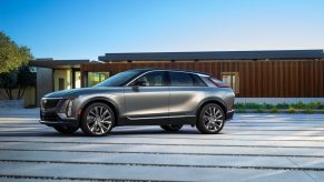 The side 3/4 view of a gray 2023 Cadillac Lyriq in front of a wood-and-glass modern building