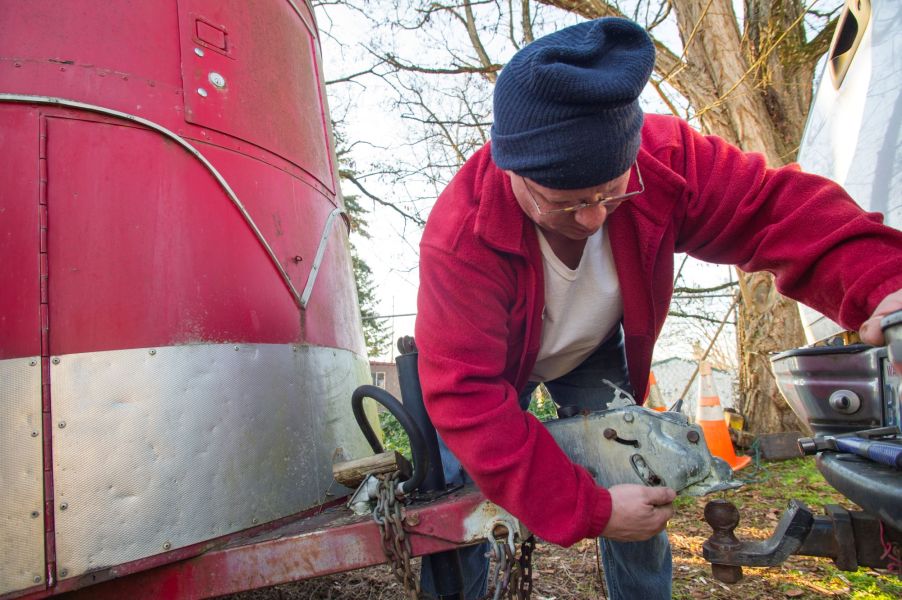 Man is attaching a red box trailer to a ball hitch that is attached to a truck.