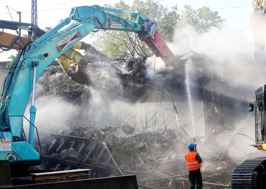 Construction workers tearing down a railway bridge with demolition equipment