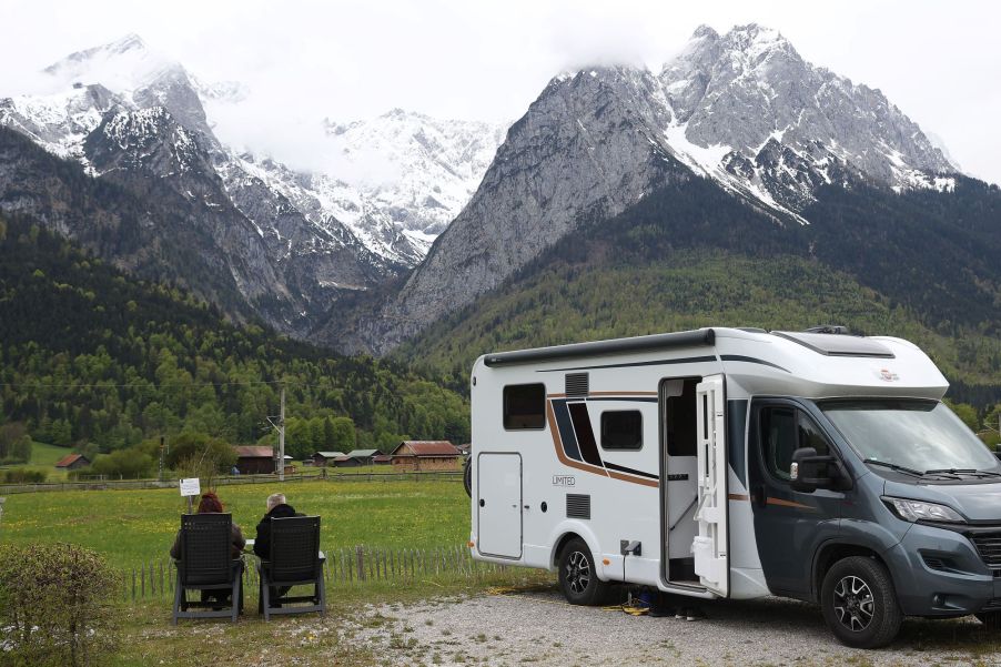 A camper van RV parked near mountains as a couple relaxes outside