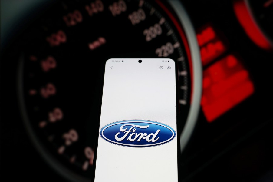 The Ford logo on a smartphone screen with a car's illumited instrumention panel in the background