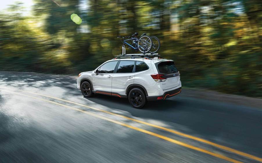 A white 2021 Subaru Forester driving down a tree-lined road.