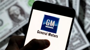 The General Motors (GM) logo displayed on a smartphone with U.S. dollars in the background