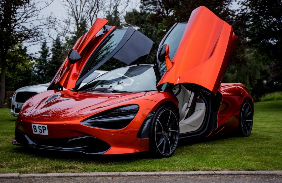 a red McLaren 720S with the doors open parked on the grass