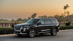 A black Hyundai SUV sits on a roadway in front of a concreate barrier with trees, water, and a sunset sky in the background.