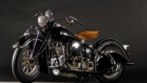 An old black Indian Motorcycle with a tan seat against a dark grey background.