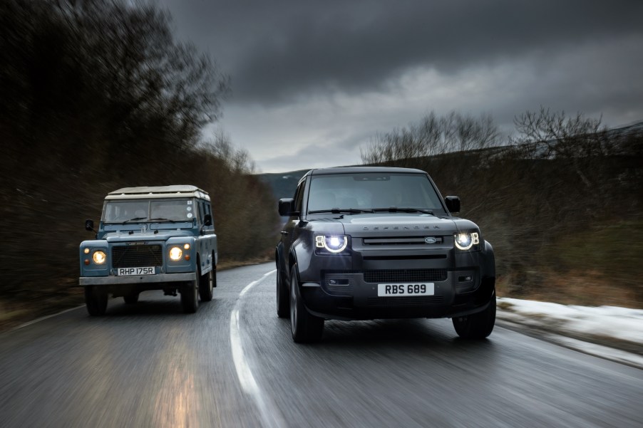 A 1977 Land Rover Defender Series III Stage One V8 and a 2021 Land Rover Defender 90 V8 travel side-by-side on a wet road