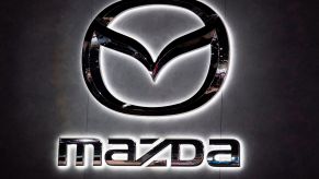 An illuminated chrome Mazda sign with Mazda written underneath the logo on black background.