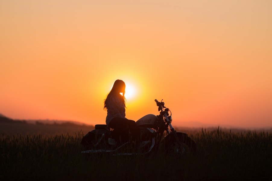 Woman watches the sunset from a motorcycle in the Adirondack mountains.