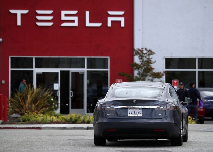 A Tesla Model S driving to a parking lot outside of a Tesla showroom