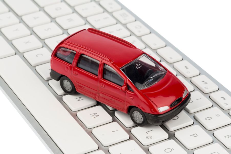 A tiny red minivan toy placed on top of an Apple keyboard