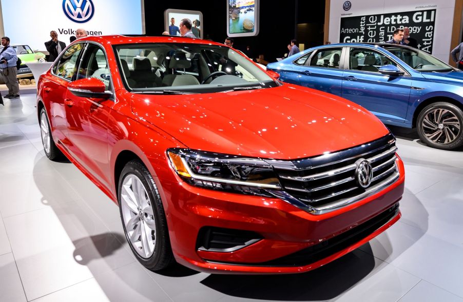 An orange Volkswagen Passat sitting in a show room on a white floor with a black and blue background.