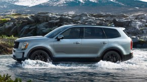 A silver 2021 Kia Telluride splashing through a river with a mountain in the background.