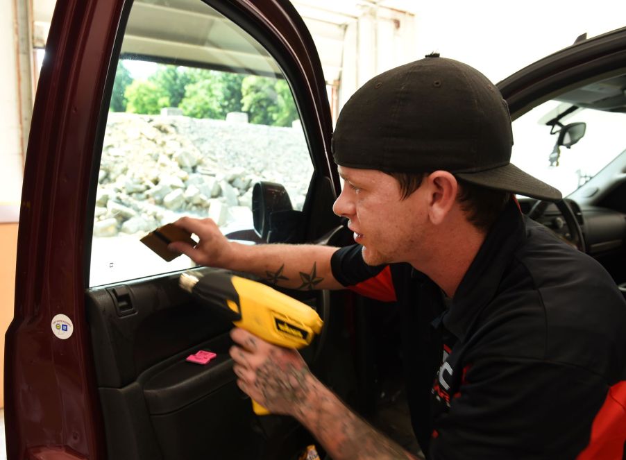 A man performing a window tinting service with a heat gun