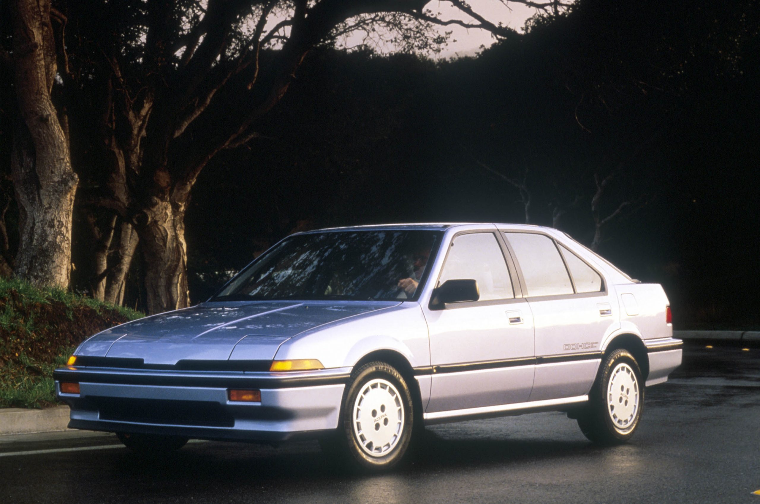 A silver 1986 Acura Integra RS shot from the 3/4 angle on a wet city street