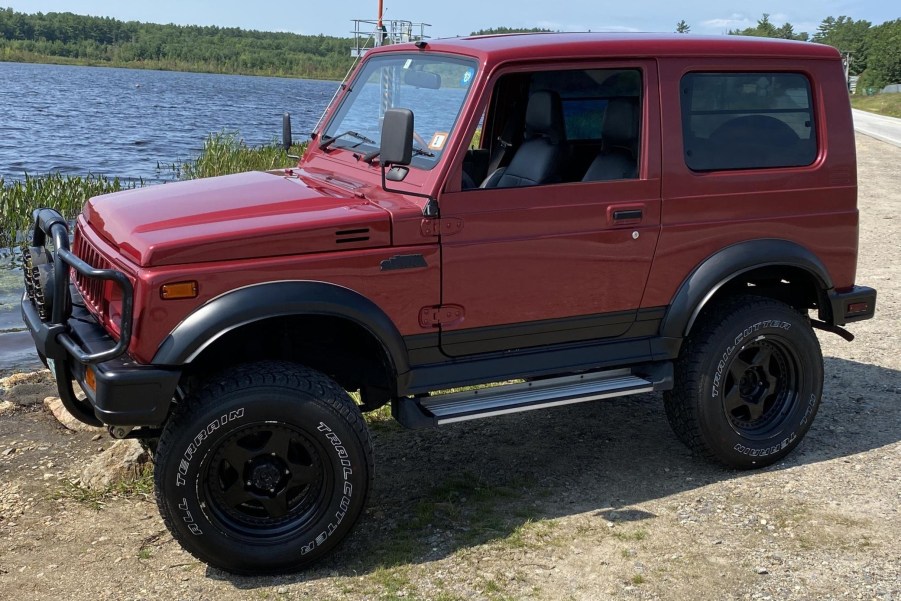 The side 3/4 view of a red 1994 Suzuki Jimny Sierra 4x4 by a lake