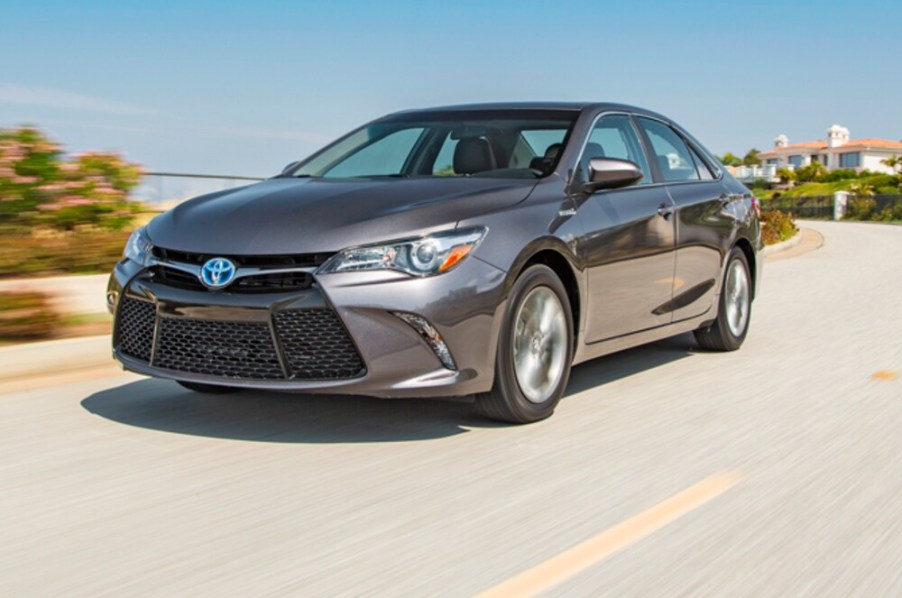 A grey 2015 Toyota Camry Hybrid driving on a sunny day