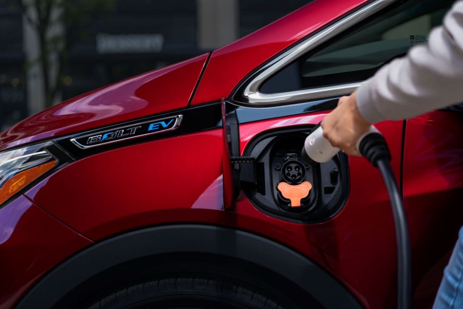 A driver about to charge their red 2020 Chevy Bolt EV model