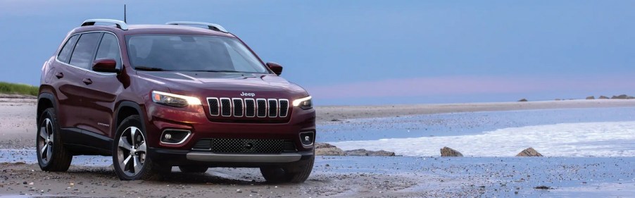 A red 2021 Jeep Grand Cherokee driving at the edge of the ocean.