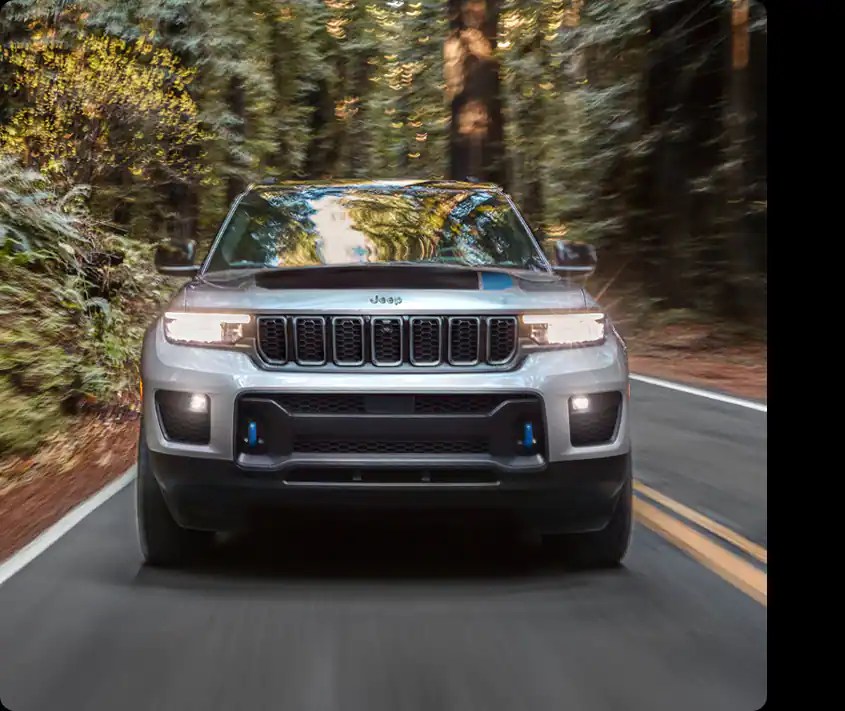 A silver 2022 Jeep Grand Cherokee 4xe driving down a wooded road.