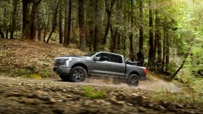 A gray 2022 Ford F-150 Lightning driving on a dirt road in a wooded area.