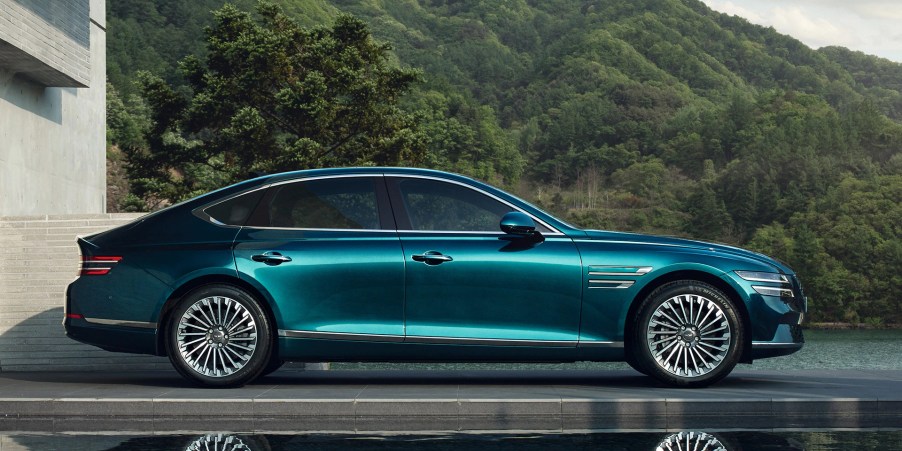 A blue 2022 Genesis Electrified G80 parked next to a tree-covered hill.