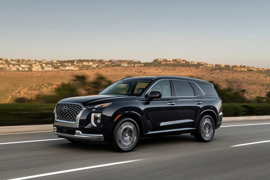 A black 2022 Hyundai Palisade travels on a highway past arid rolling hills on a sunny day