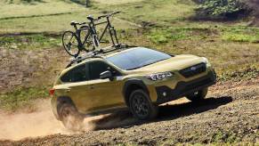 A yellow 2021 Subaru Crosstrek with a bike on top drives on a dirt road