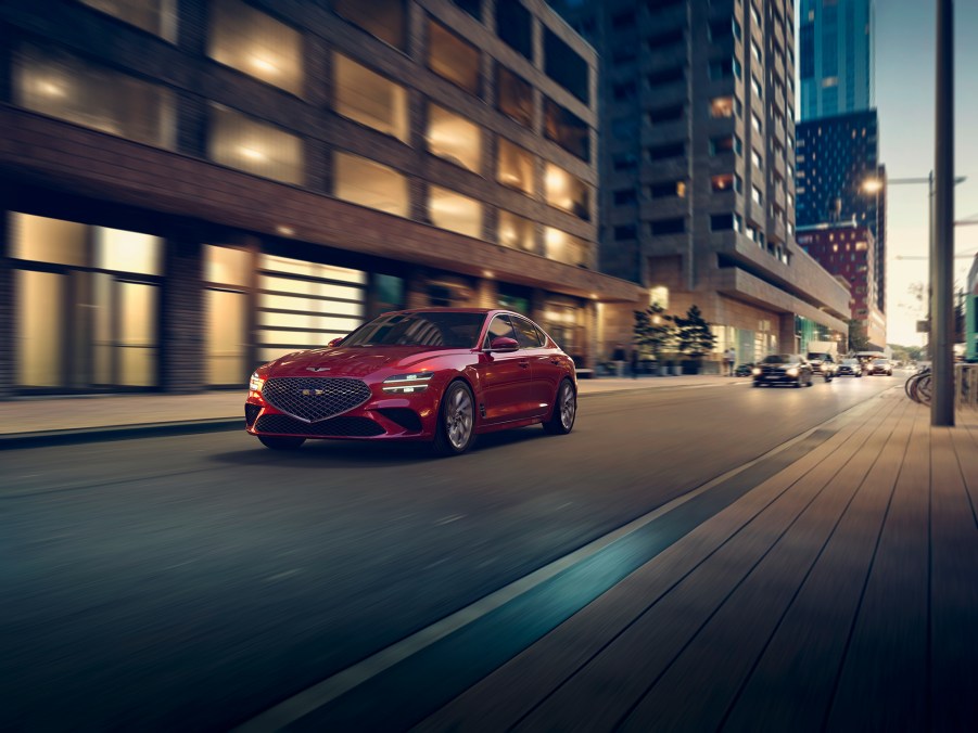 A red 2022 Genesis G70 rolling down a city street at night shot from the front 3/4