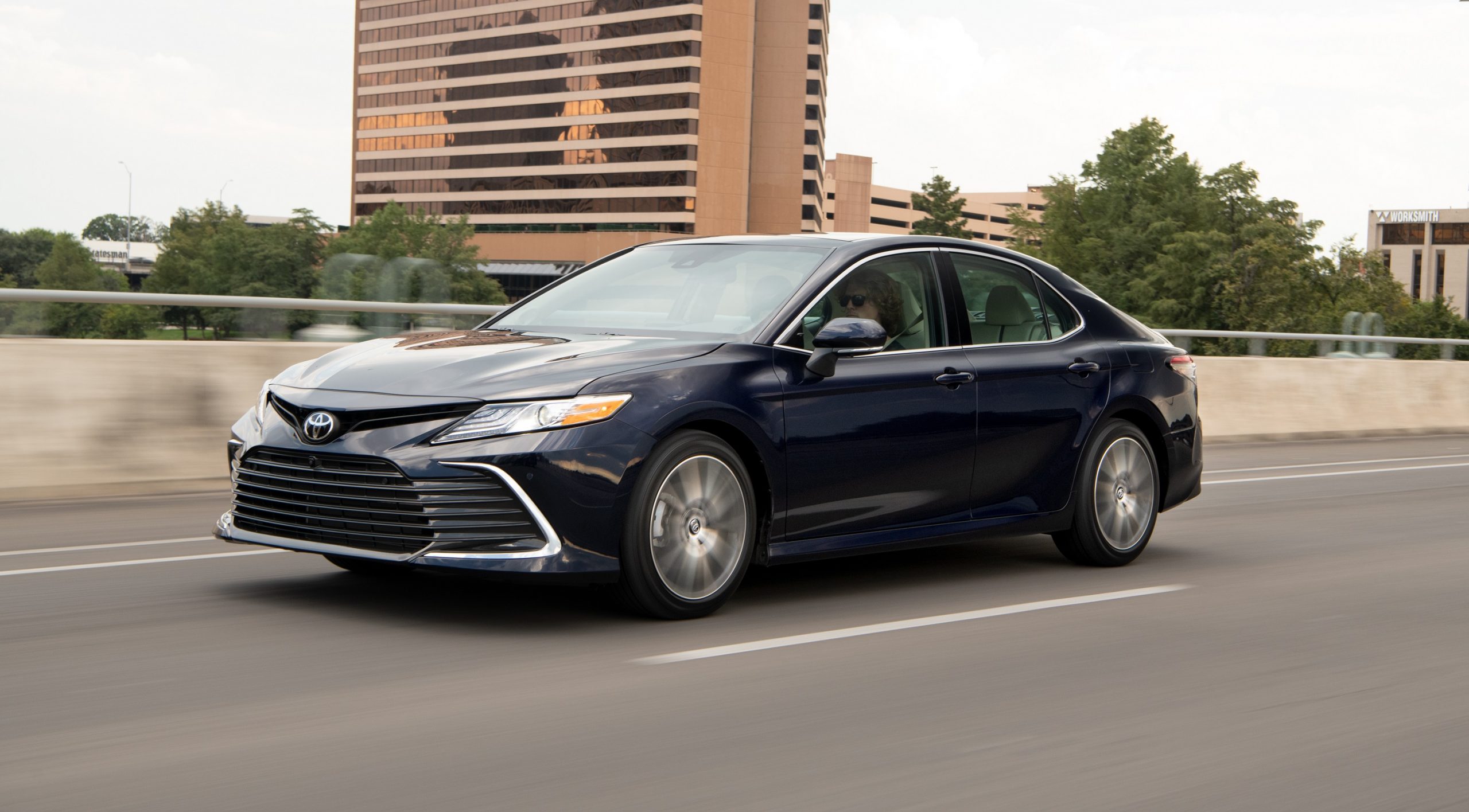 A blue Toyota Camry, shot from the front 3/4 rolls down the highway